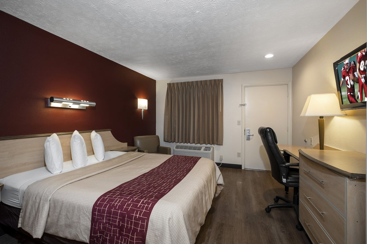 A hotel room with a bed, a desk, a chair, a TV, and a lamp.