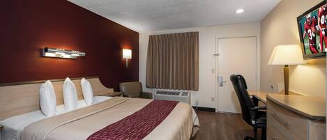 A hotel room with a bed, a desk, a chair, a lamp, a TV, and a window with curtains.