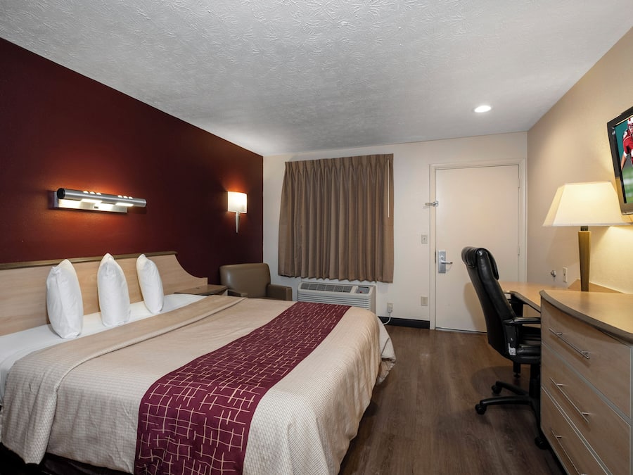 A hotel room with a bed, a desk, a chair, a lamp, a TV, and a window with curtains.