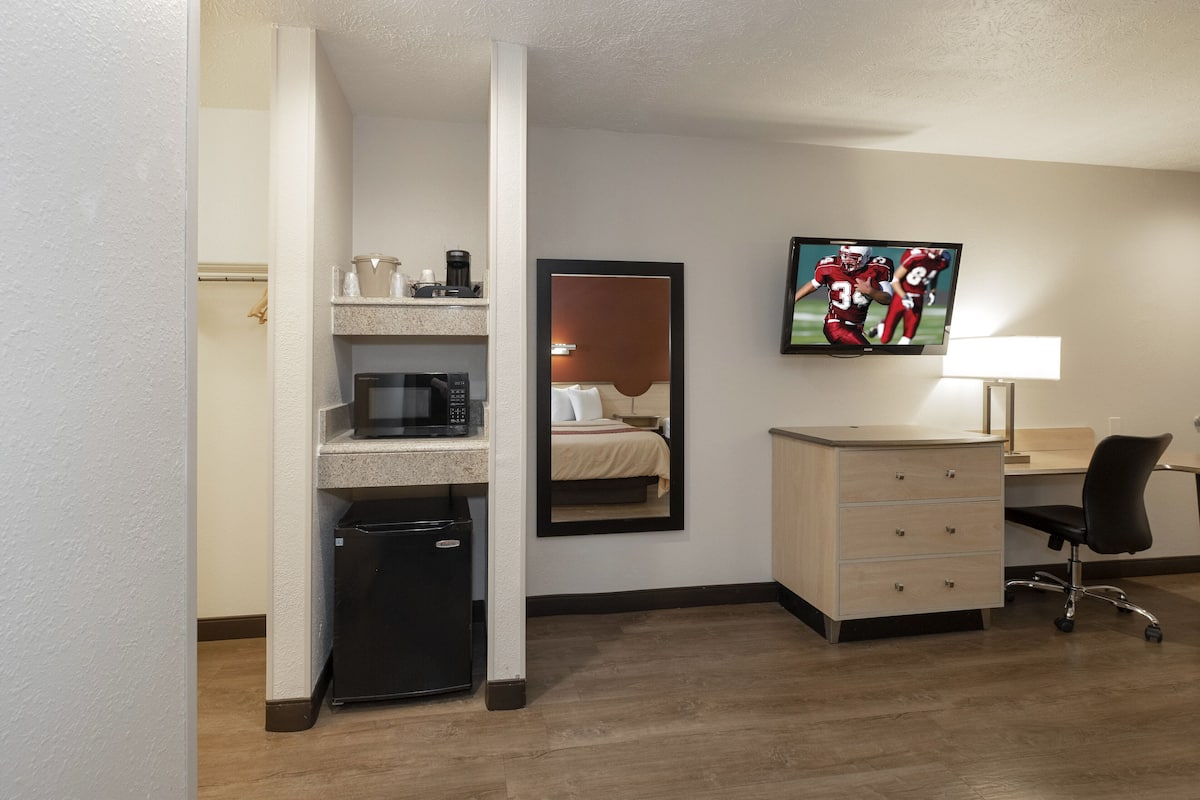 A hotel room with a kitchenette, a bed, a TV, a desk, and a chair.