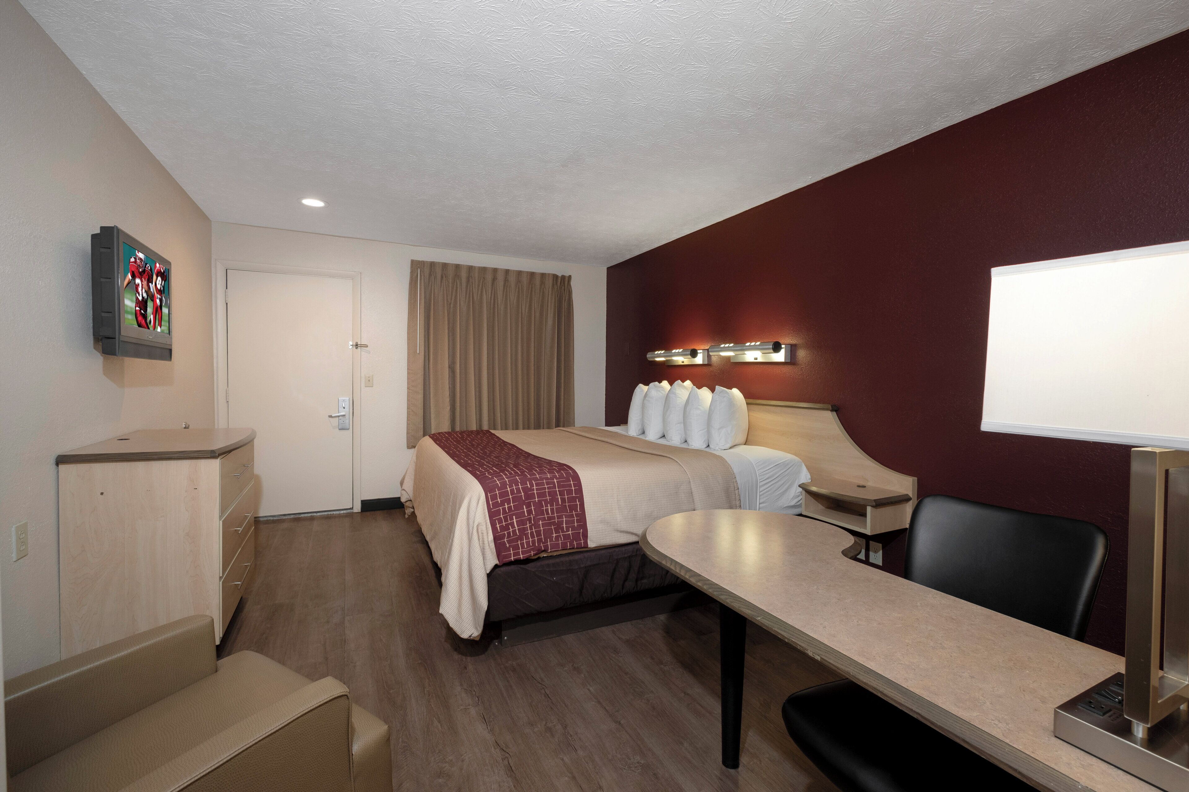Habitación de hotel con cama, escritorio, silla y televisor montado en la pared.