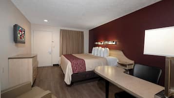 Habitación de hotel con cama, escritorio, silla y televisor montado en la pared.