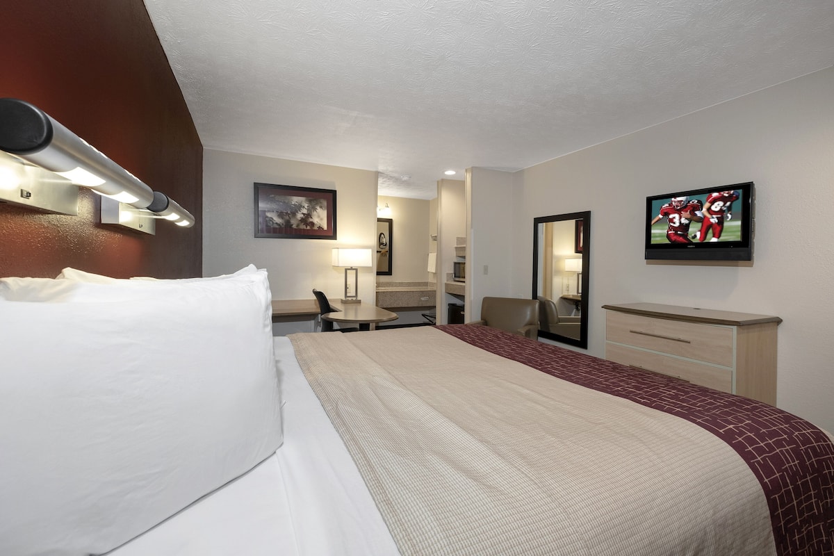A hotel room with a large bed, a desk, a chair, a TV, and a mirror.