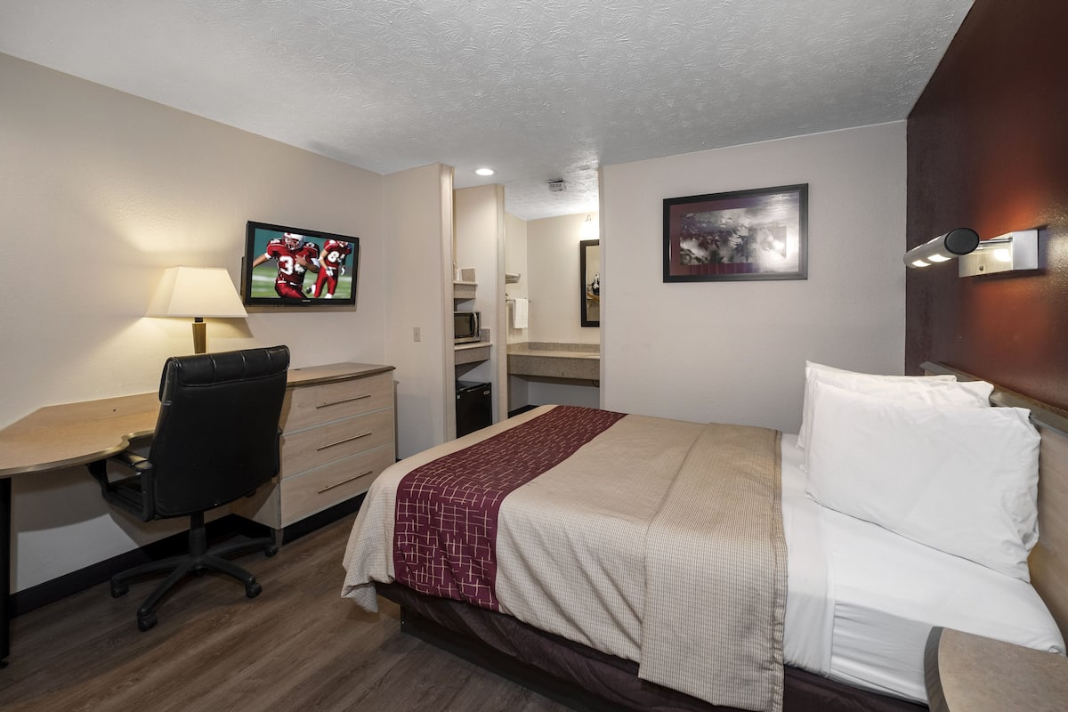 A hotel room with a bed, desk, chair, and a television on the wall.