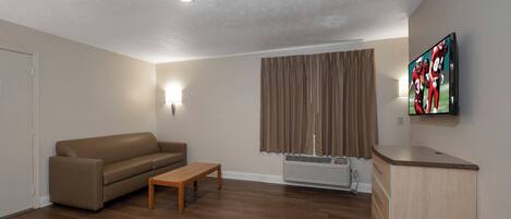 A living room with a sofa, a coffee table, a TV mounted on the wall, and a window with curtains.