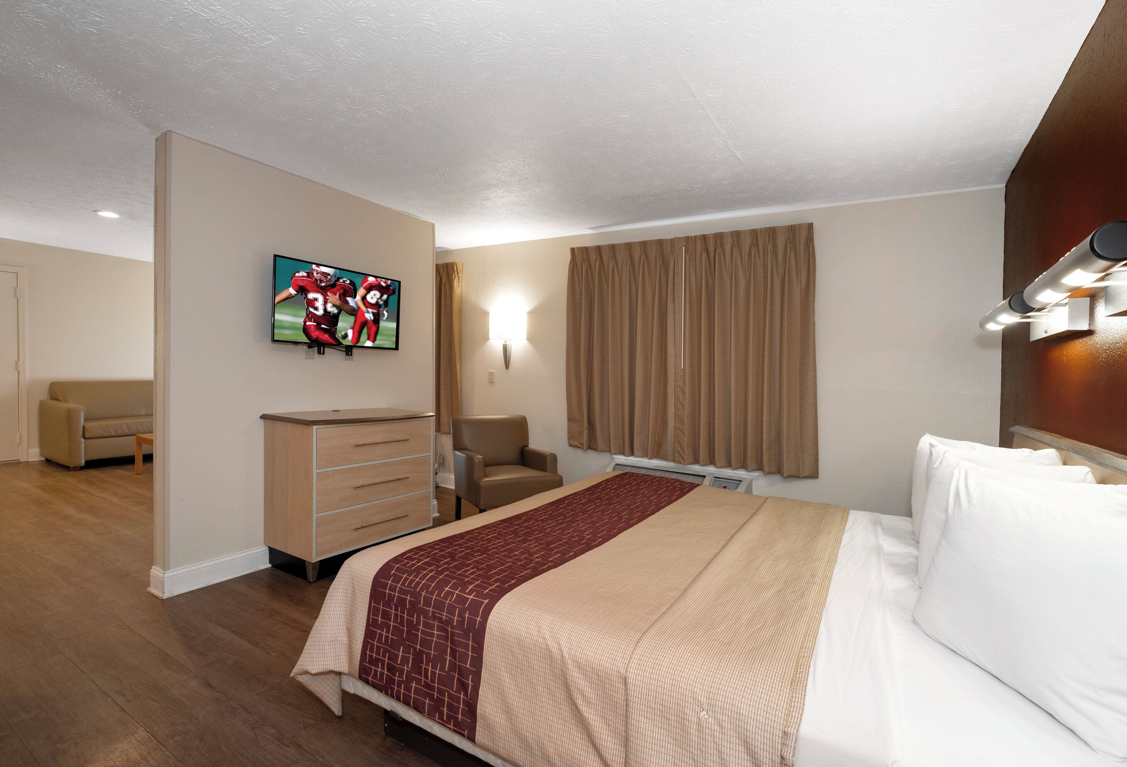 Une chambre d’hôtel avec un lit, un téléviseur fixé au mur, un bureau, une chaise et une fenêtre avec des rideaux.