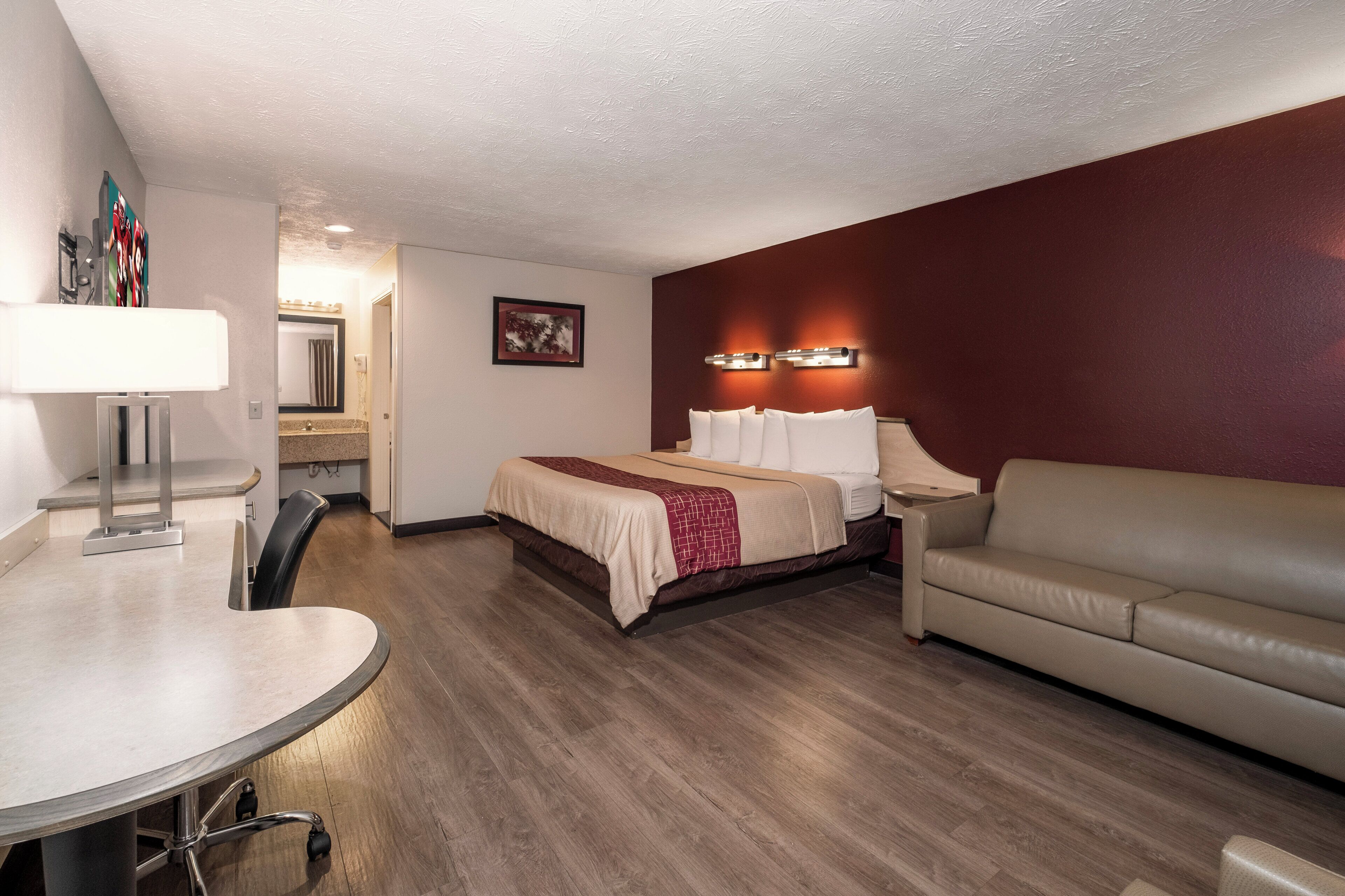 A hotel room with a bed, a sofa, a desk with a chair, and a bathroom visible through an open door.
