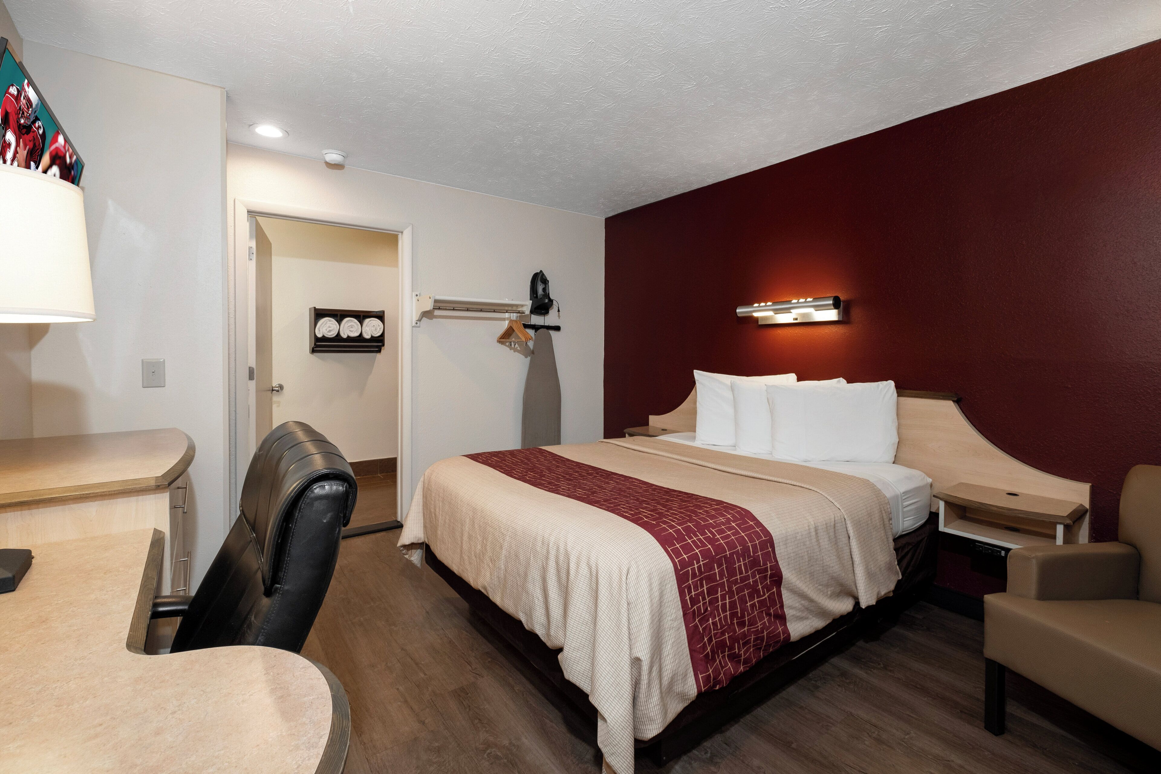 Habitación de hotel con cama, escritorio, silla, armario y una tabla de planchar fijada a la pared.