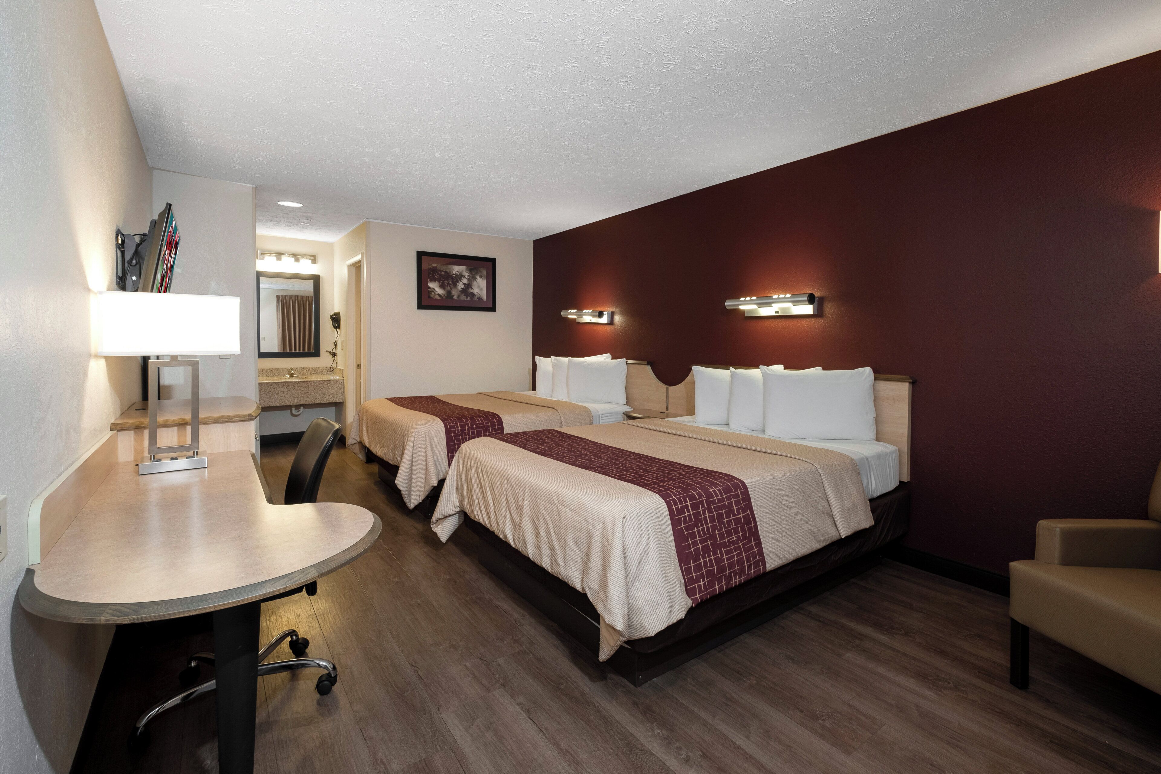 A hotel room with two beds, a desk, a chair, a mirror, and a bathroom.