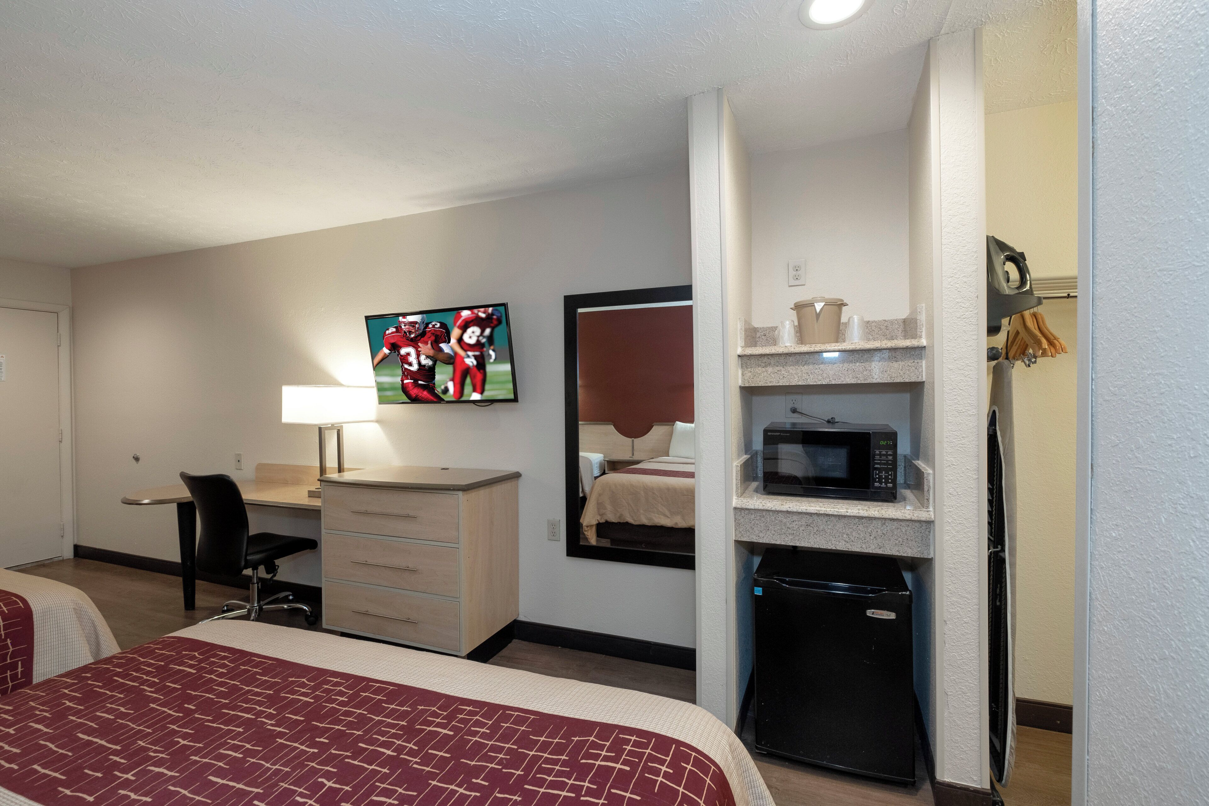 A hotel room with two beds, a desk, a chair, a television, a microwave, and a refrigerator.