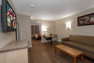 A hotel room with a TV, a sofa, a desk, a chair, a bed, and a painting on the wall.
