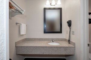 Un baño con lavamanos de encimera de granito, un espejo, toallero y secador de pelo en la pared.