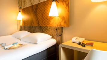Een hotelkamer met een bed, een nachtkastje met een telefoon en een bril, en een tijdschrift op het bed.