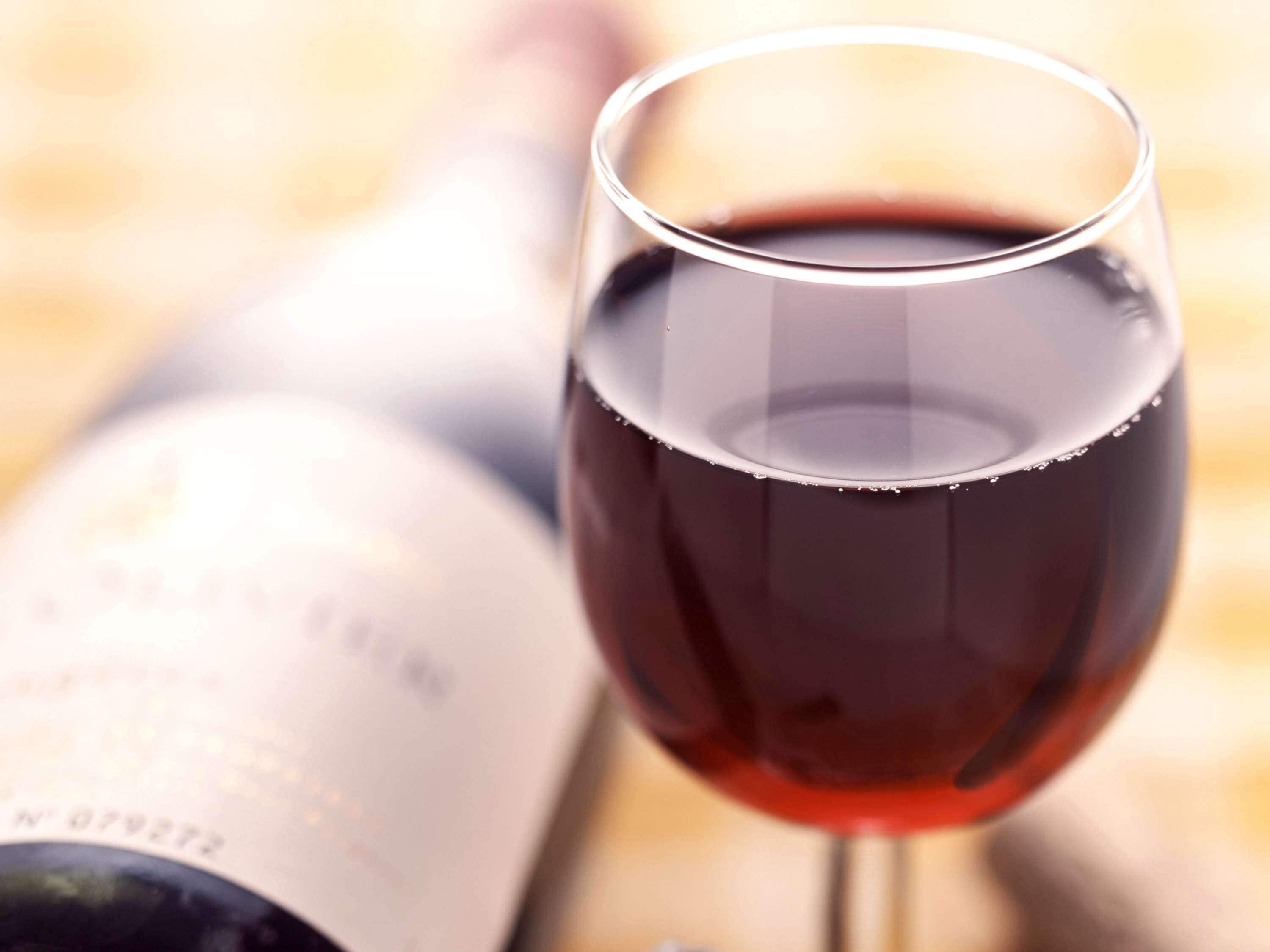 A wine glass filled with red wine, placed in front of a blurred background.