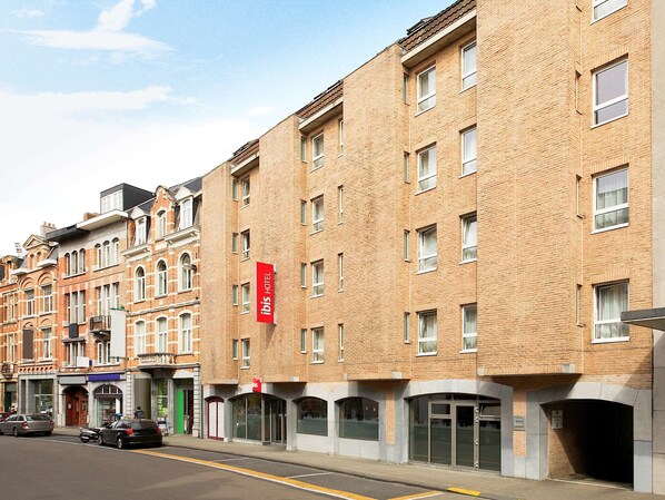 A hotel with a red sign, multiple windows, and a brick facade.