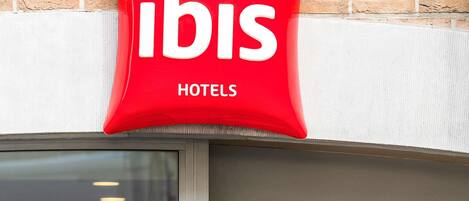 Un letrero rojo con la palabra 'ibis' y 'HOTELS', indicando el nombre del hotel.