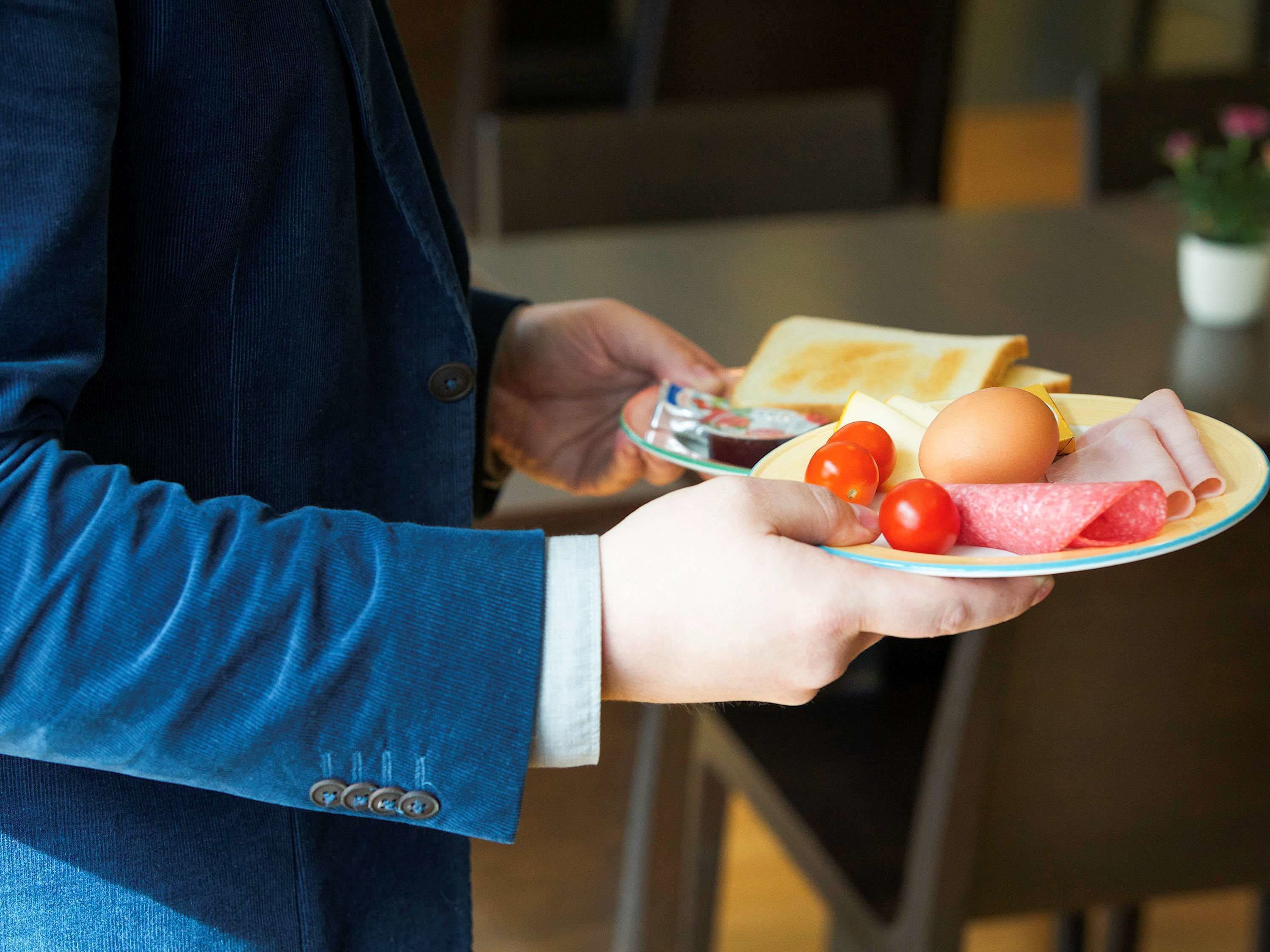 A person holding a plate with food items including bread, eggs, tomatoes, and meat.