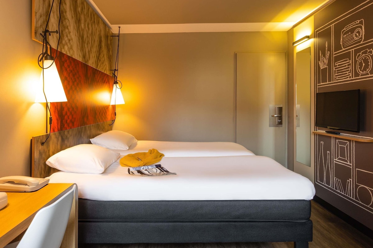 Ett hotellrum med en säng, ett nattduksbord, en lampa och en tv som är monterad på väggen.