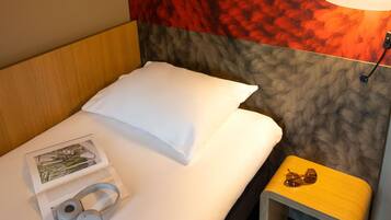 A neatly made bed with a white pillow, a magazine, and a pair of headphones on the bed.