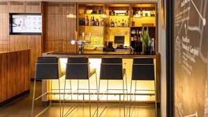 Uma área de bar moderna com armários de madeira, balcão e quatro banquetas pretas.