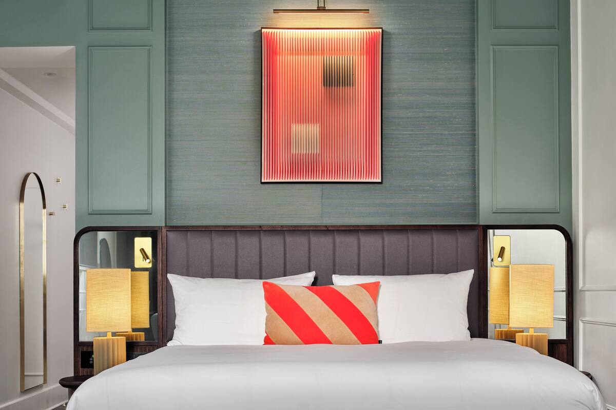 Een net opgemaakt bed met een gestreept kussen, een bedlampje en een wandlamp.