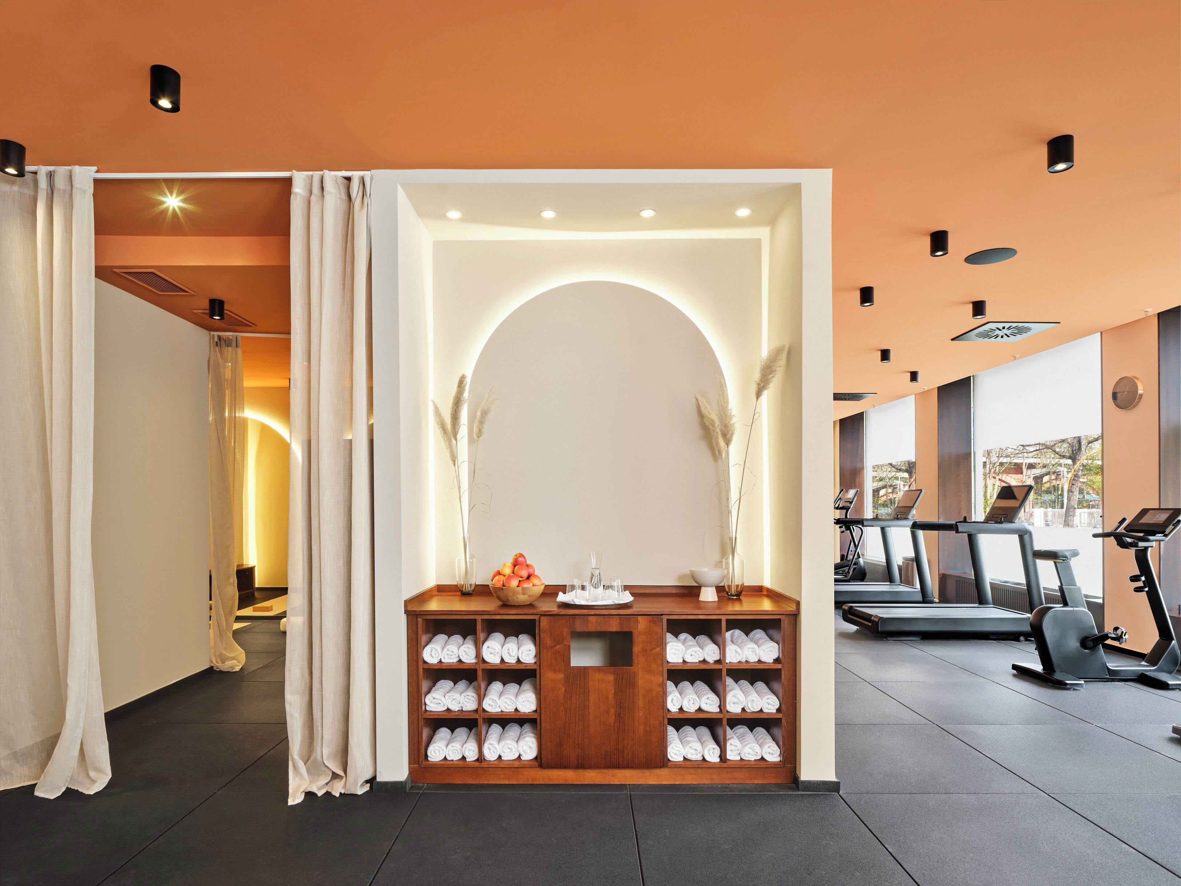 A gym with exercise equipment, a reception desk with towels, and a view of the outdoors.