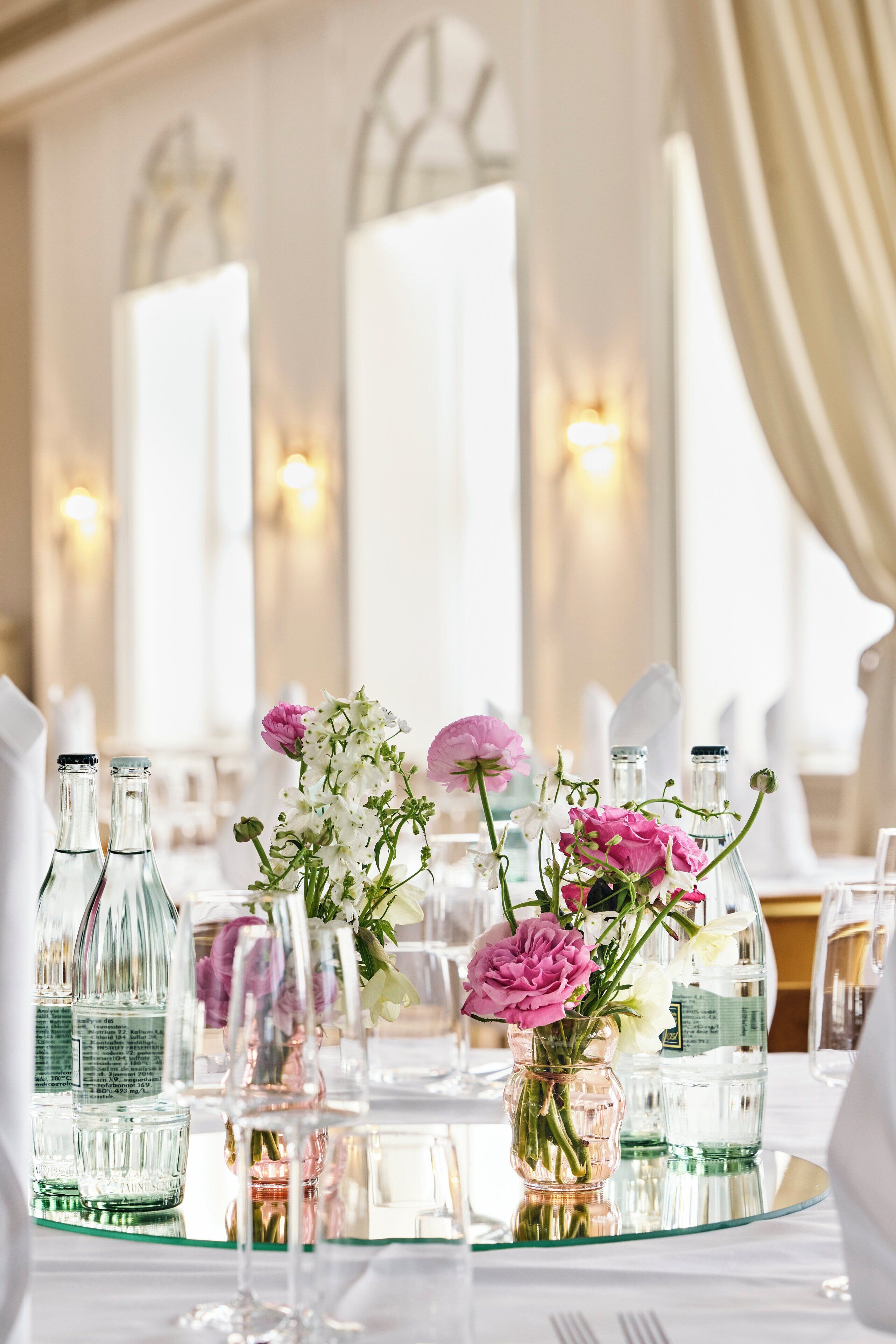 A table set with clear glass bottles, a glass vase with flowers, and a glass tray.
