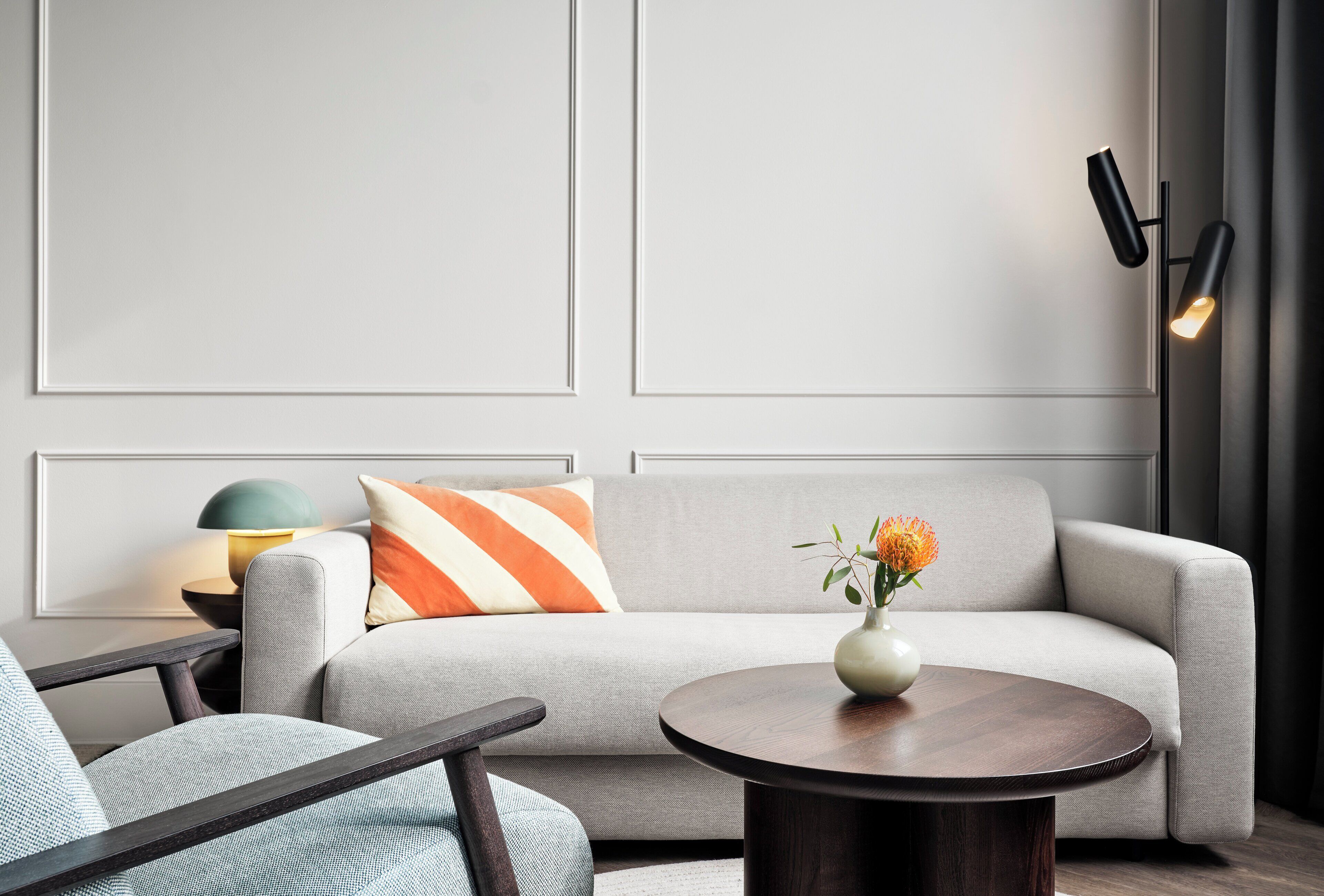 A modern living room with a grey sofa, a round wooden coffee table, and a side table with a lamp.