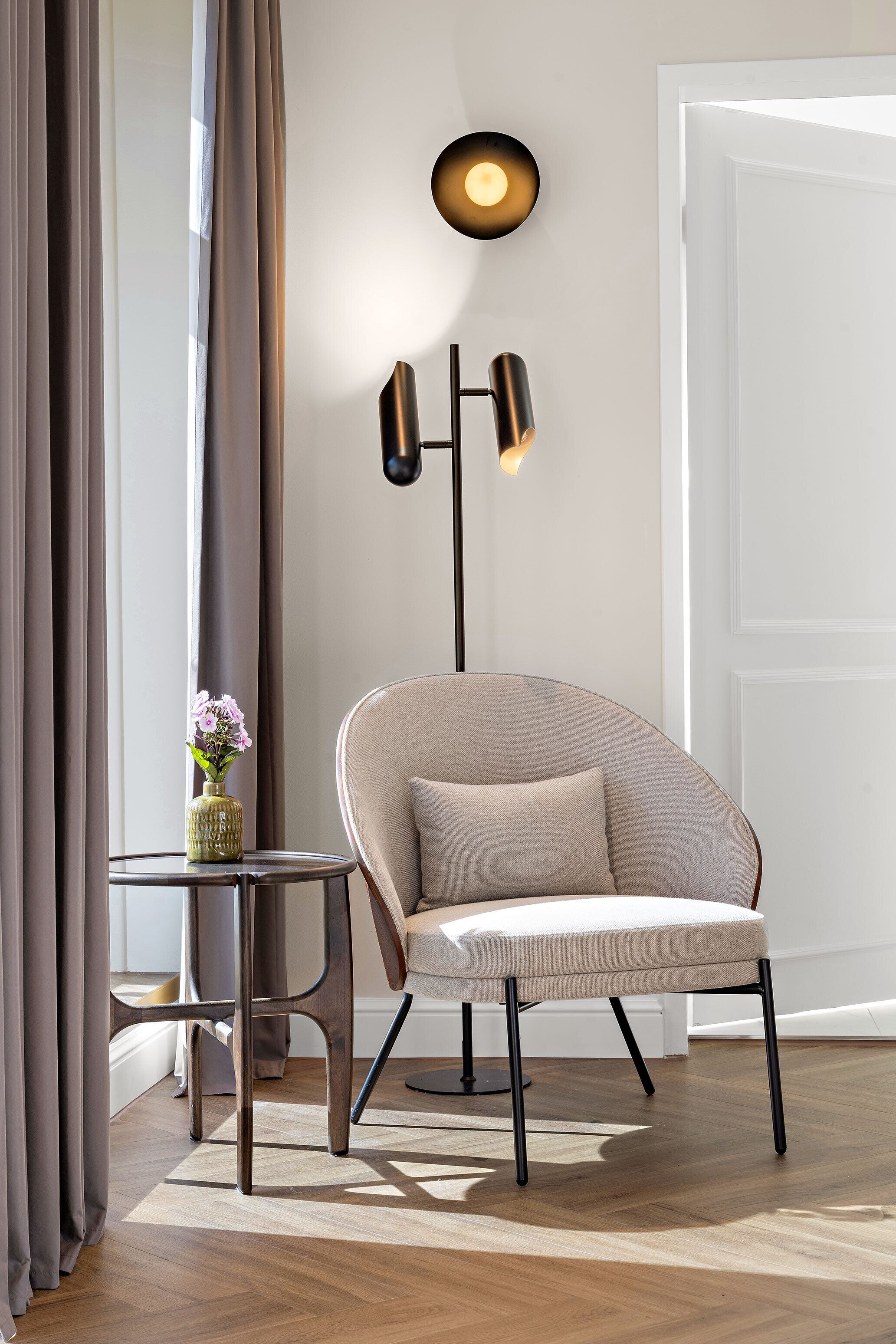 A modern room with a light-colored armchair, a small side table with a vase, and a floor lamp.