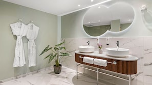 Un baño moderno con dos lavamanos, un espejo grande y dos albornoces blancos colgados en ganchos.