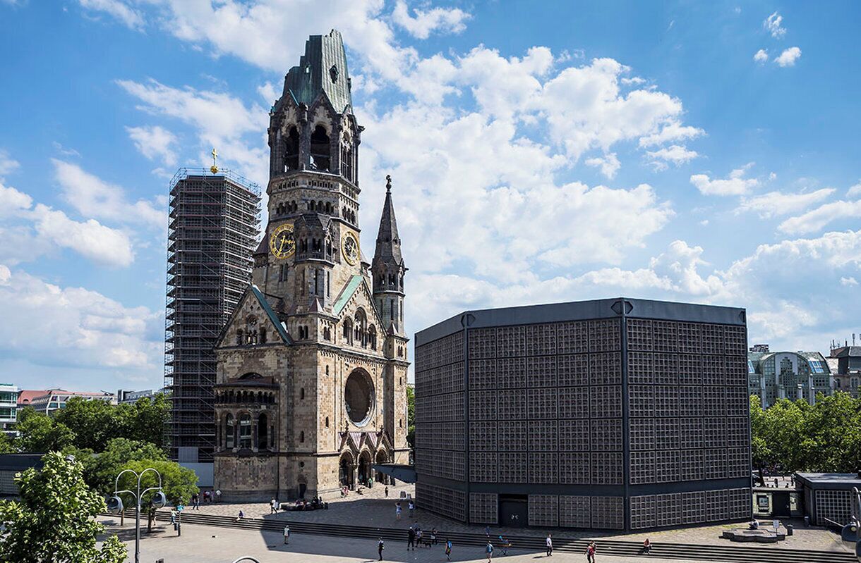 Una iglesia histórica con torre del reloj y un edificio moderno de fachada enrejada.