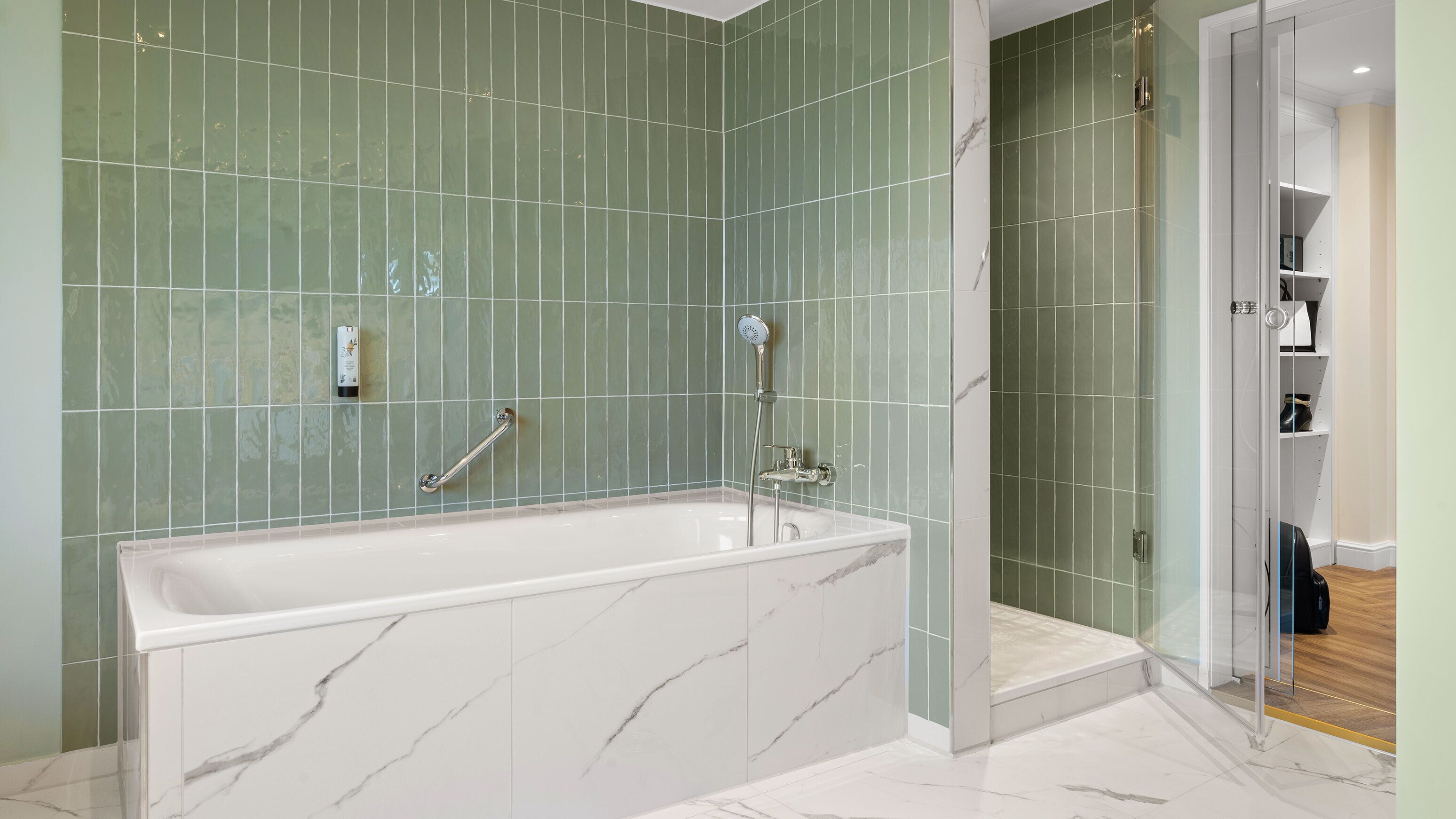 Ein modernes Badezimmer mit einer Marmorbadewanne, grünen Fliesenwänden und einer Duschkabine aus Glas.