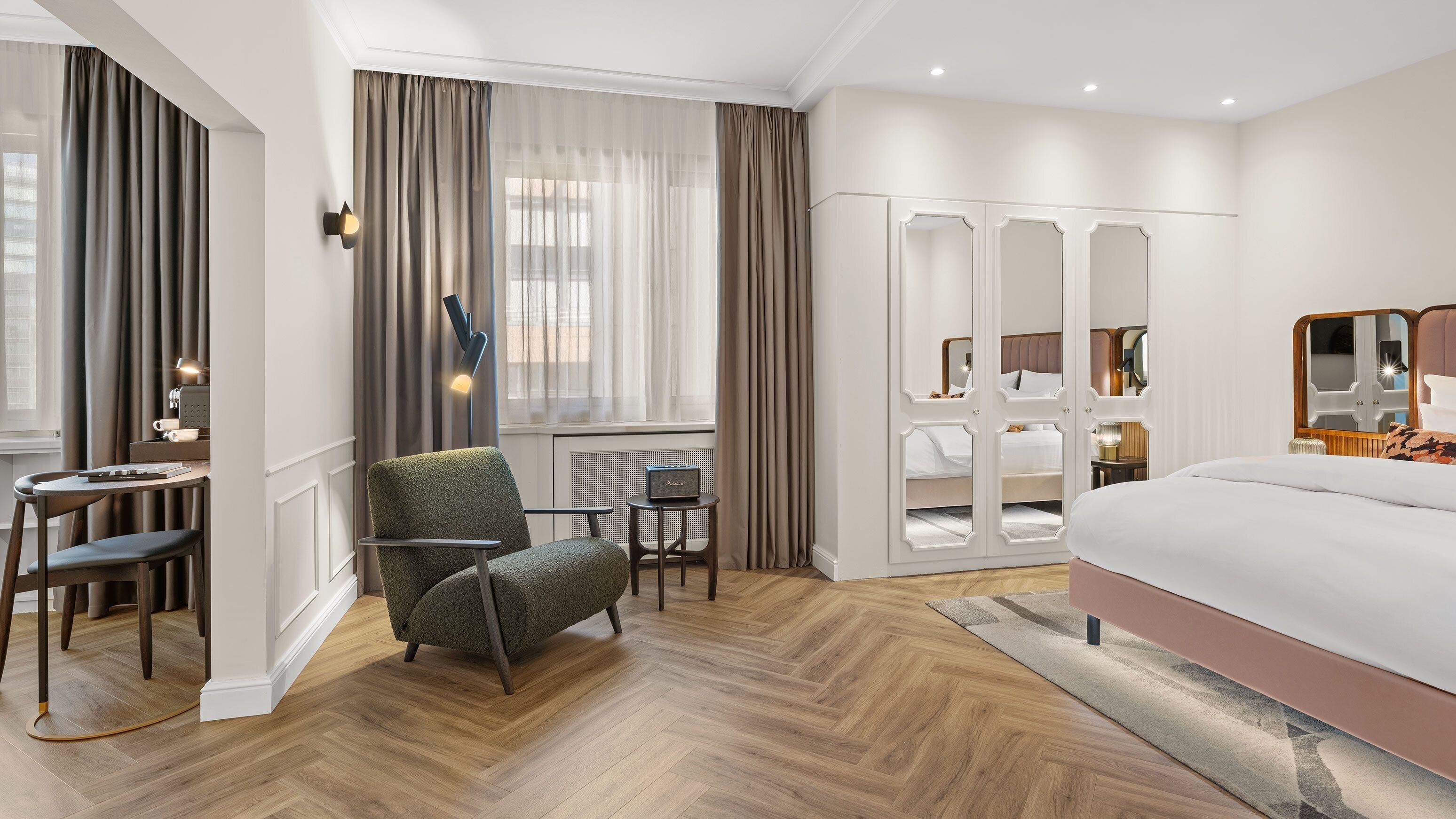 Una camera d'albergo con un letto, una scrivania con una sedia, un tavolino e una finestra con tende.