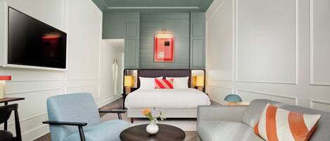 A hotel room with a bed, a TV, a chair, a sofa, a coffee table, and a wall-mounted lamp.
