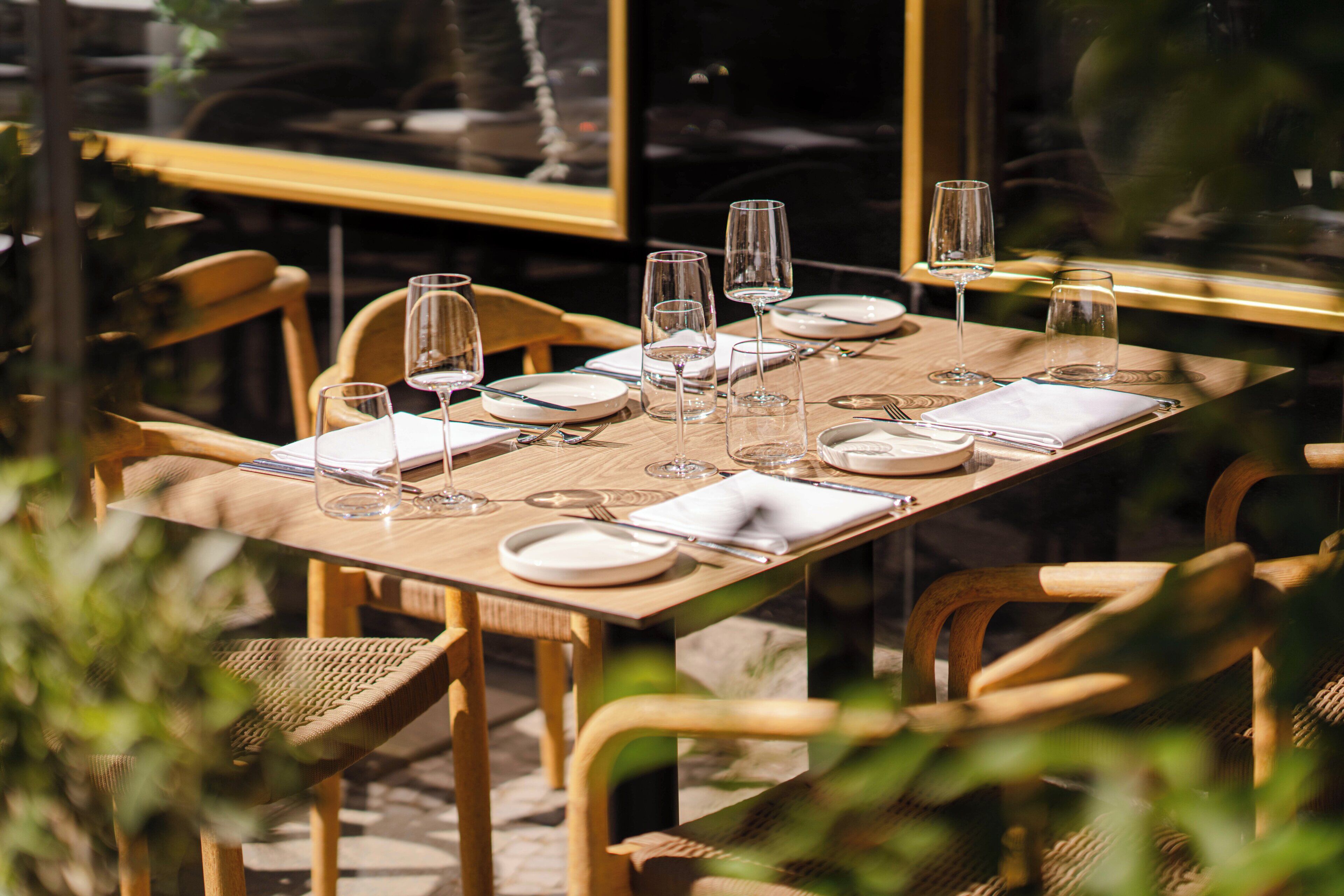 A dining table set with plates, cutlery, and wine glasses, surrounded by wicker chairs.
