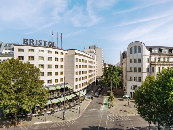 Un hotel con un llamativo letrero 'BRISTOL', un patio central con mesas al aire libre y una vista de la calle con coches estacionados.