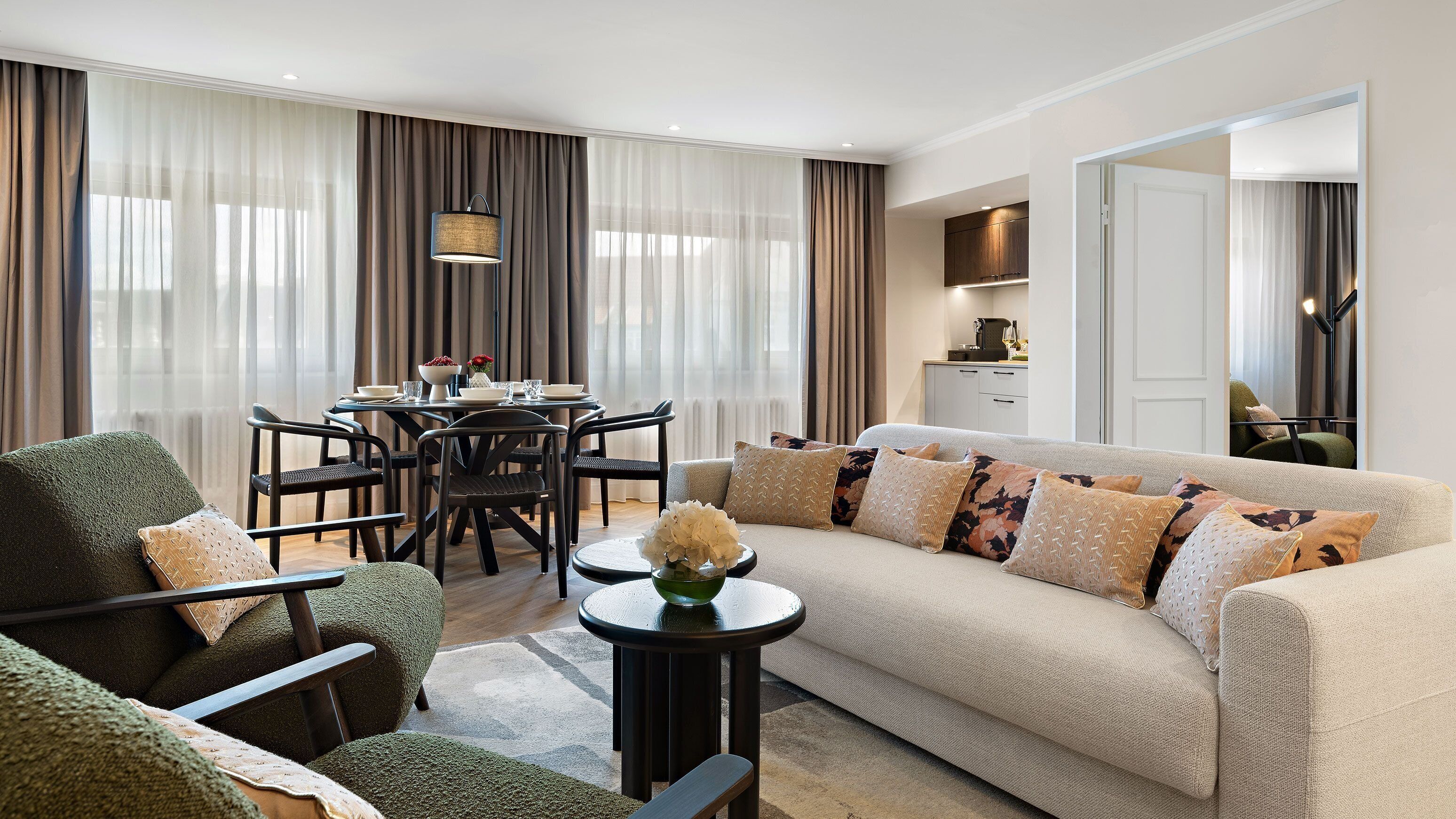 Un salon moderne avec un canapé, des fauteuils, une table à manger et un coin cuisine à l’arrière-plan.