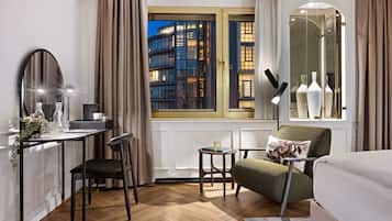 A modern hotel room with a desk, chair, and a view of a cityscape through a large window.