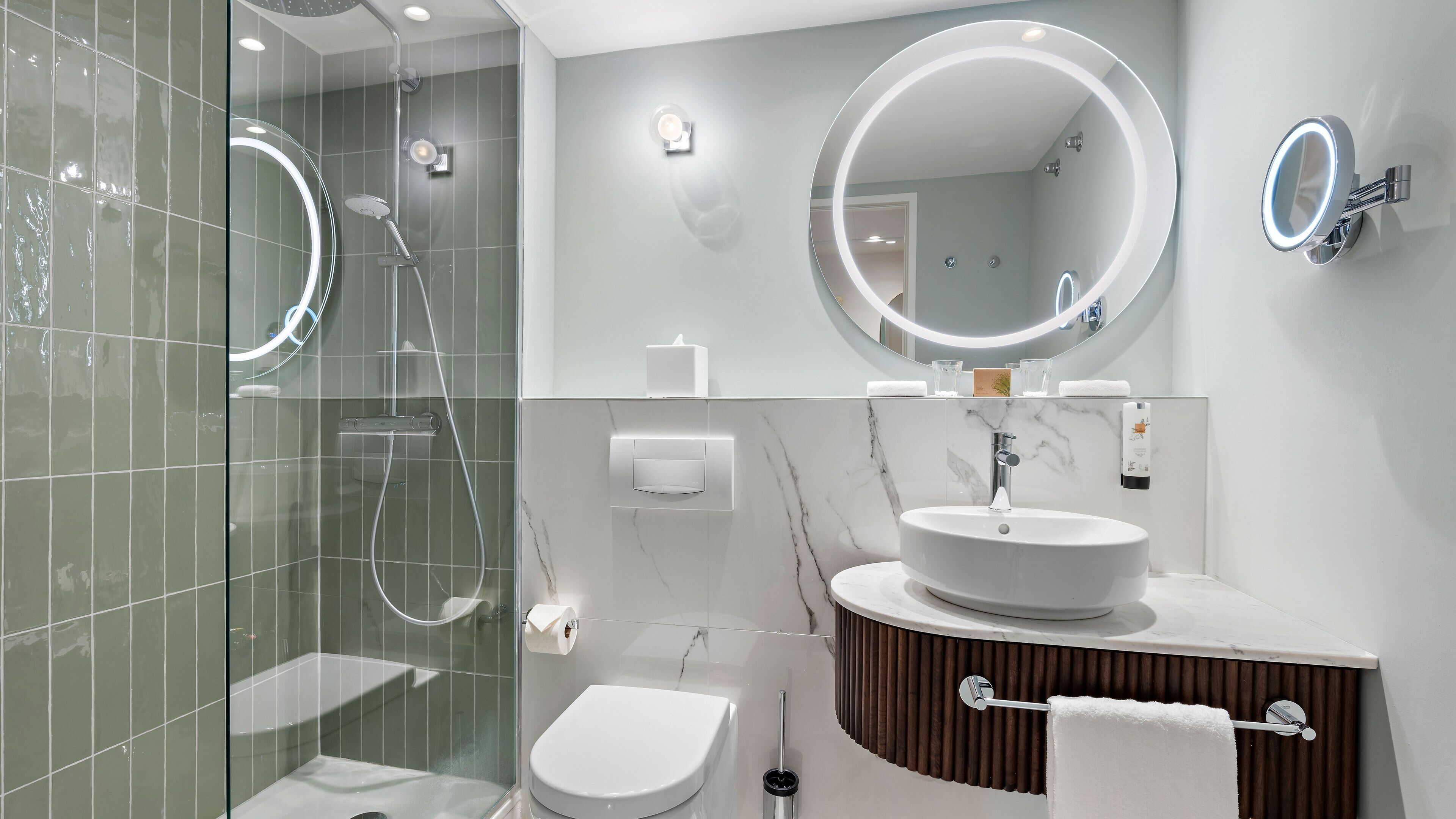 Un baño moderno con ducha de vidrio, lavamanos blanco con encimera de mármol y un espejo grande sobre el lavamanos.