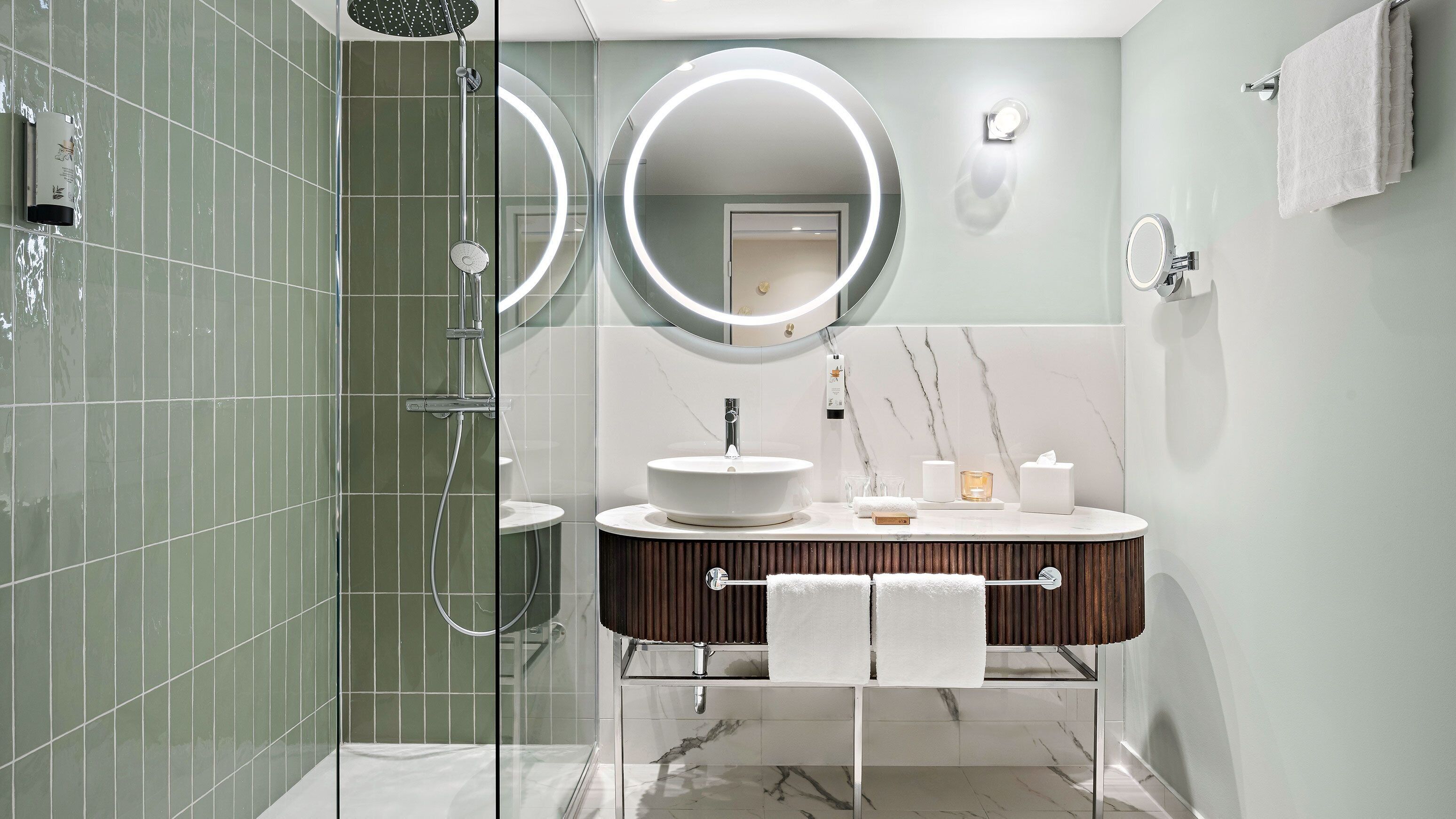 Une salle de bain moderne dotée d’une douche à parois de verre, d’un meuble-lavabo avec un plan de travail en marbre et de deux miroirs fixés au mur.