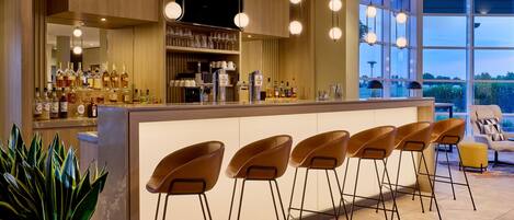 A bar area with a long counter, multiple stools, and a variety of bottles.