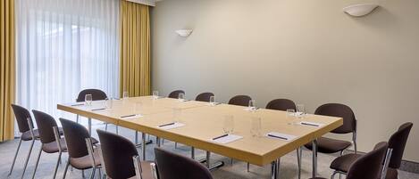 A conference room with a long table, multiple chairs, and a large window with curtains.