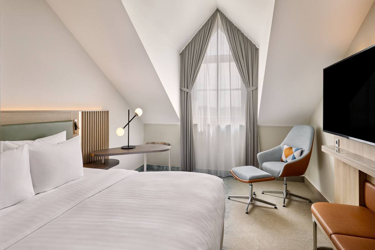 Une chambre d’hôtel avec un grand lit, un bureau avec une lampe, une télévision et une chaise.