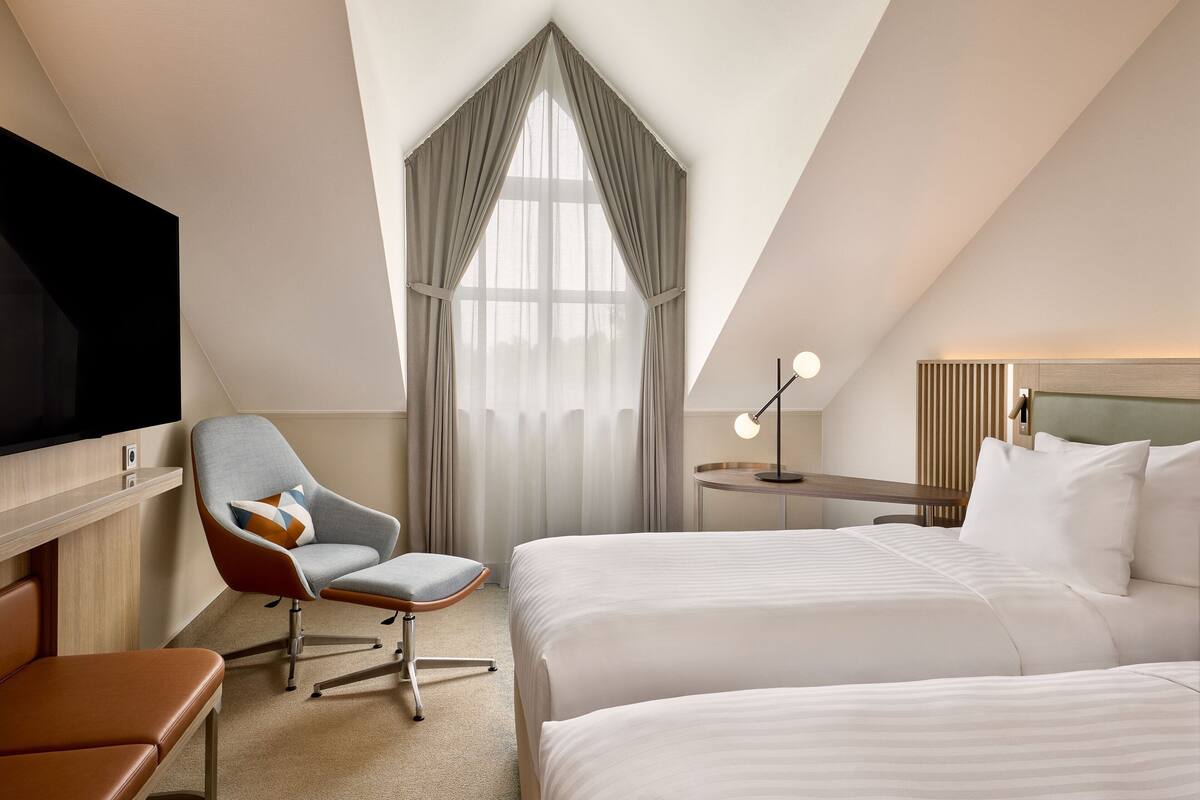 Une chambre d’hôtel avec un grand lit, un bureau, une chaise, une télévision et une fenêtre avec des rideaux.