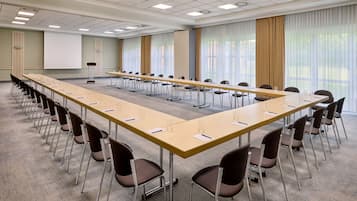 A conference room with a long table, chairs, a projector screen, and large windows with curtains.