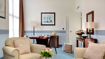 Habitación de hotel con dos sillones, una mesita con un florero, un escritorio con lámpara y un cuadro en la pared.