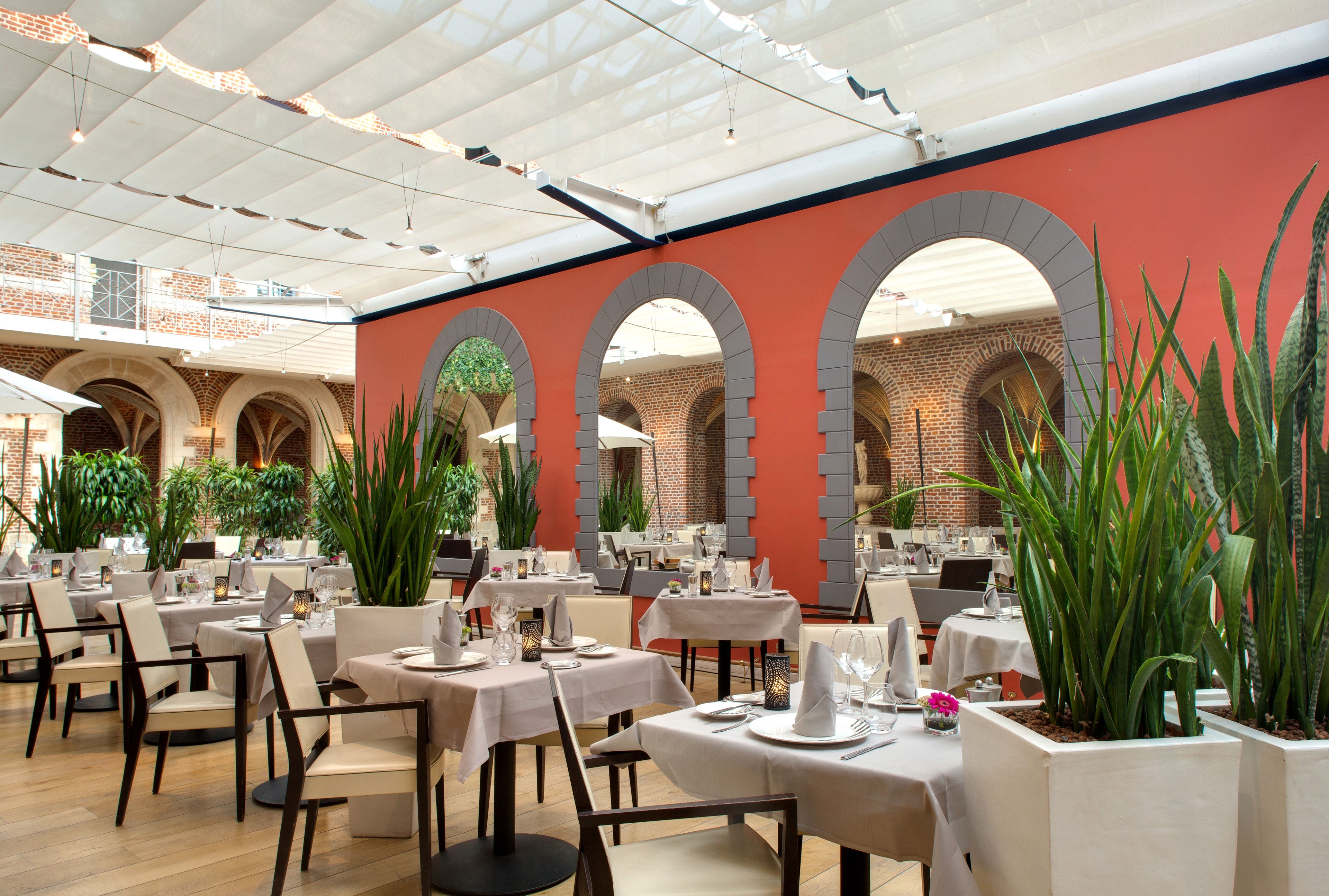 Een restaurant met meerdere tafels en stoelen, bakstenen muren en grote potplanten.