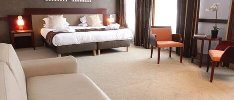 A hotel room with a large bed, a sofa, a chair, and a small table with a plant.