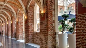 A spacious corridor with brick walls and arched ceilings, large potted plants, and a modern interior design.