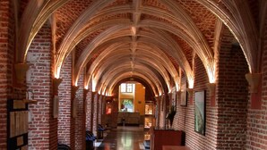 A long corridor with arched brick ceilings and a polished floor, leading to a seating area with blue cushions.